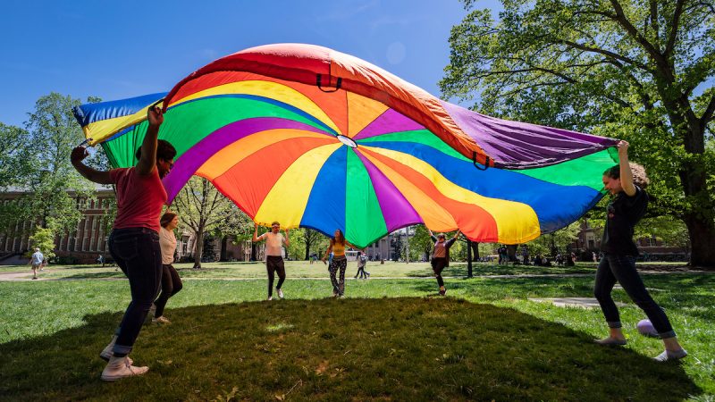 People playing with a rainbow-colored parachute
