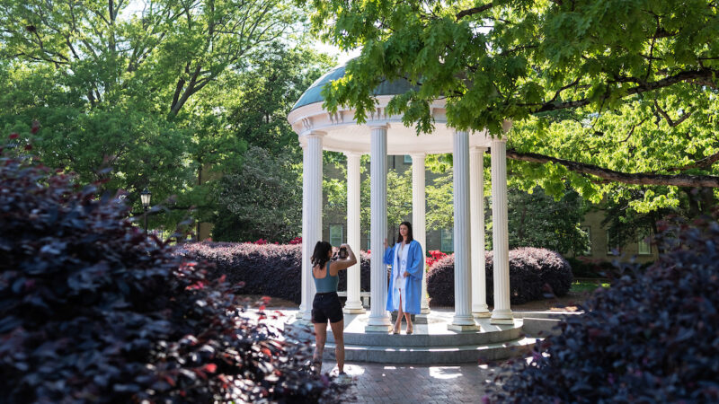 A person takes a graduation photo at the Old Well on the UNC-Chapel Hill campus.