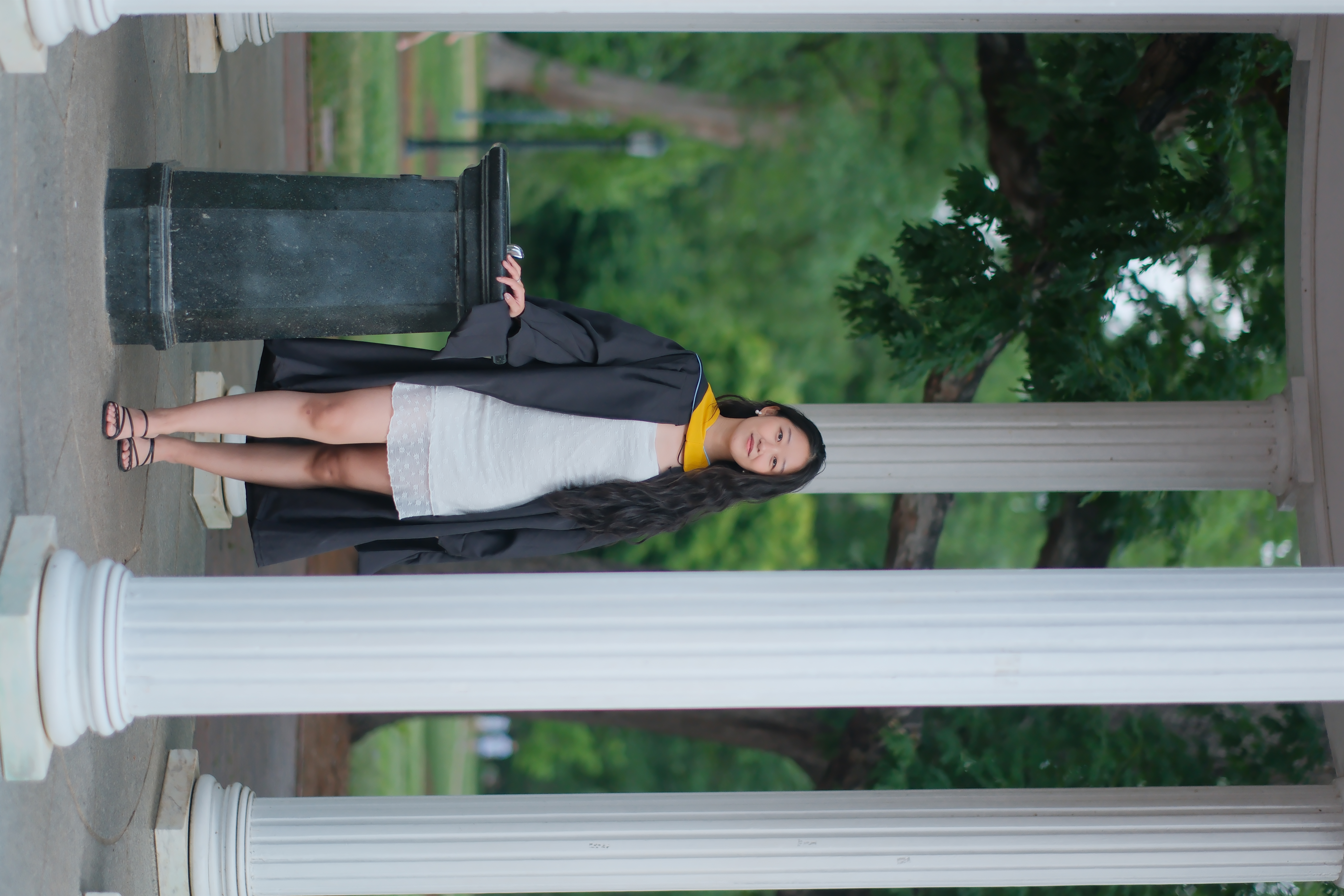 A student poses by the Old Well wearing master's degree graduation regalia.