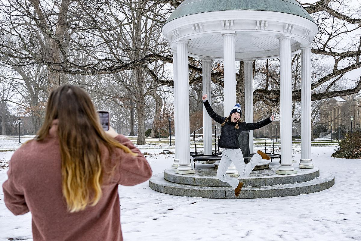 Snow falls on the campus of the University of North Carolina at Chapel Hill on January 16, 2022. In this image, senior Laurenne Losier jumps in front of the Old Well while having her picture made by friend and fellow senior Blake Ryan.
